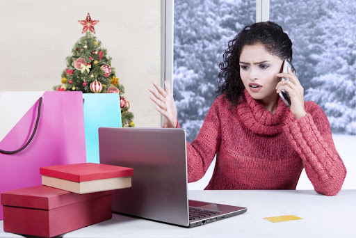 Portrait of angry Indian woman talking on the phone while complaining after shopping online with laptop and shopping bags on desk